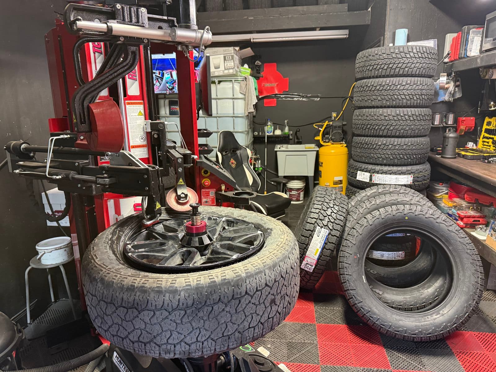 Truck tire on the Hunter Revolution tire changer beside a stack of new all-terrain tires