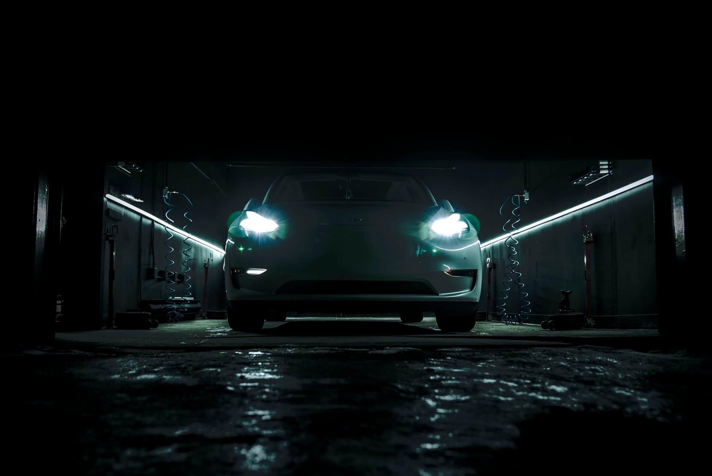 Tesla Model 3 headlights illuminating a wet floor inside the dark PitStop & Go service bay