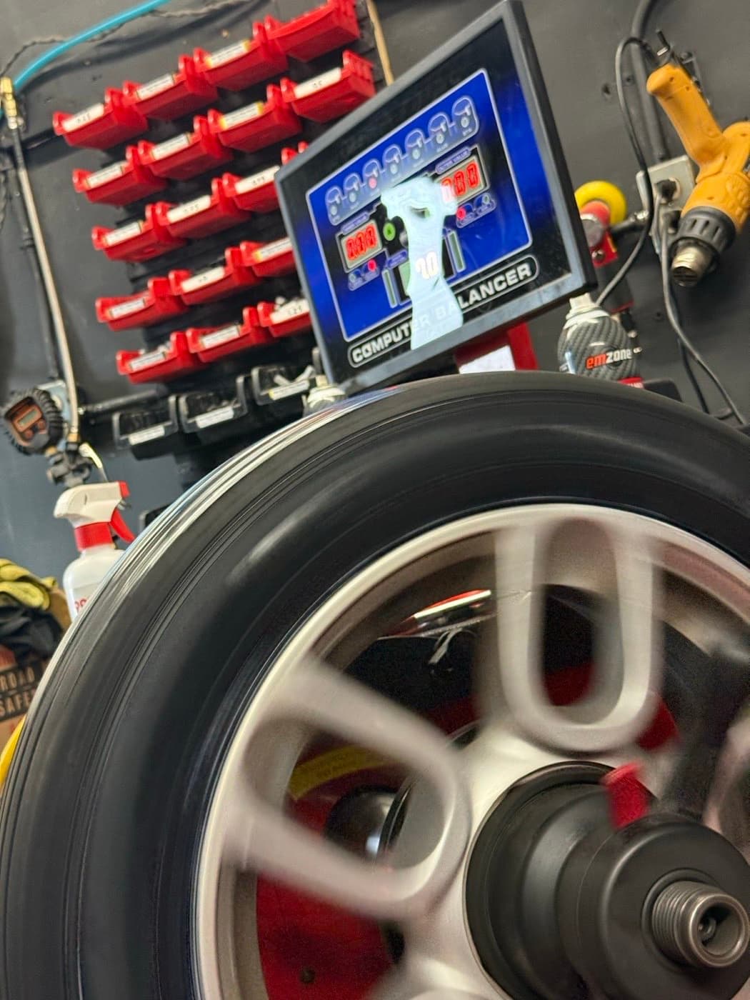Alloy wheel spinning on the computer balancer at PitStop & Go, with the readout above it and a rack of clip-on weights on the wall behind