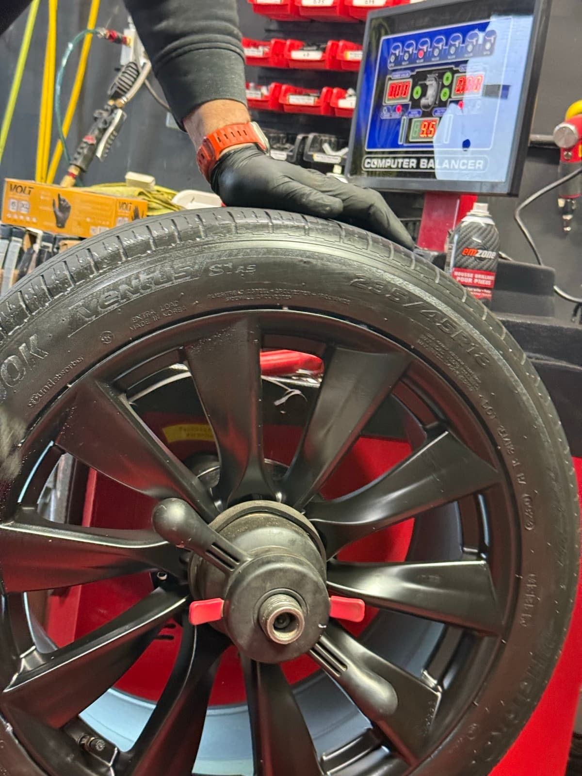 Technician mounting a 12-spoke black wheel on the tire machine